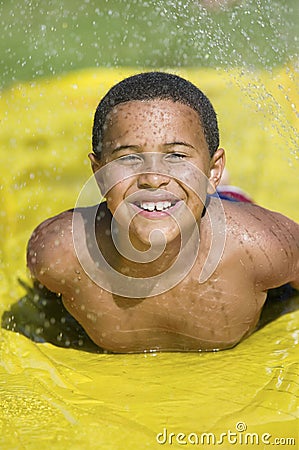 Boy (7-9) sliding on water slide front view portrait. Stock Photo