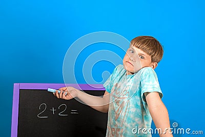 The boy solves the math equation 2 + 2 written on the blackboard. The child does not know the answer to simple examples Stock Photo