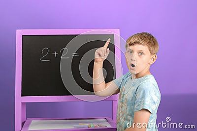 The boy solves the math equation 2 + 2 written on the blackboard. The child holds his finger up Stock Photo