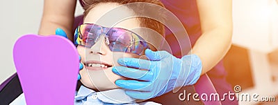 A boy in special glasses in the dentist`s chair. the doctor in sterile gloves shows him his smile in the mirror Stock Photo