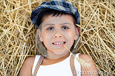 Boy with a spikelet in the teeth lies on the hay. Stock Photo