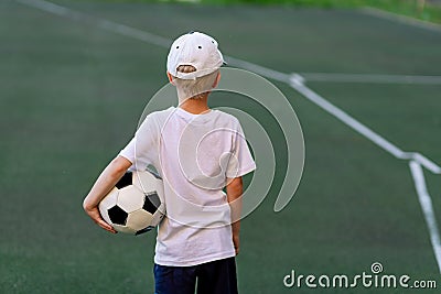 A boy in sports clothes sitting on a green lawn on a football field with a soccer ball back, back view, sports section, training Stock Photo