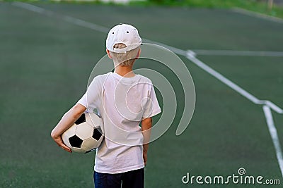 A boy in sports clothes sitting on a green lawn on a football field with a soccer ball back, back view, sports section, training Stock Photo