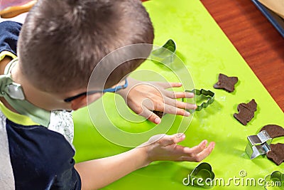 Boy squeezes the shapes from the molds on the rolled brown dough. Pressed shapes are next to prepared for bakin. Stock Photo