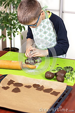 Boy squeezes the shapes from the molds on the rolled brown dough. Pressed shapes are next to prepared for baking. Stock Photo