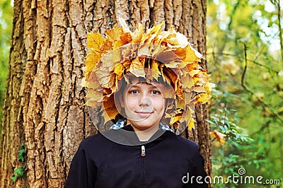 Boy standing in autumn park on a background of trees. At the head of woven wreath of autumn leaves Stock Photo