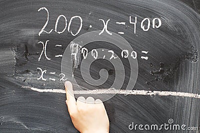 Boy standing back in front of school blackboard and writing. Schoolboy solves math example at the chalkkboard Stock Photo