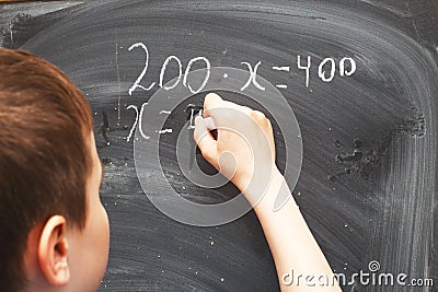 Boy standing back in front of school blackboard and writing. Schoolboy solves math example at the chalkkboard Stock Photo