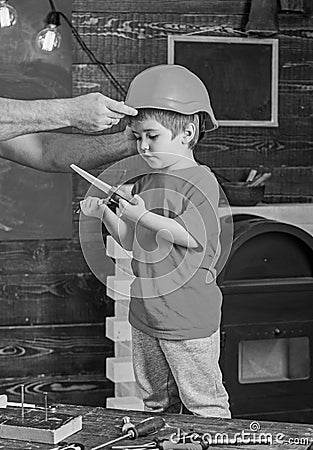 Boy standing behind the table with various tools. Daddy taking care about sons safety. Male hands holding orange Stock Photo
