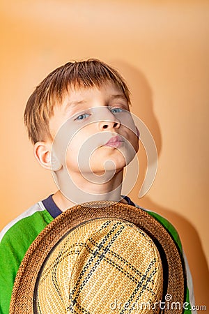 A boy in a straw hat and green clothes on a beige background takes off his hat in greeting Stock Photo