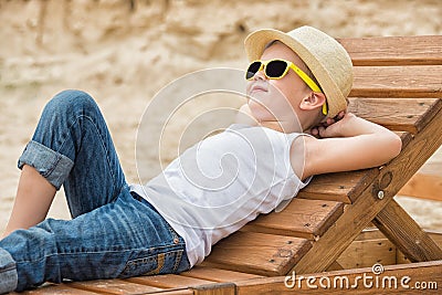 The boy in the straw hat lying on the wooden sun loungers on the beach.Summer vacation. Stock Photo