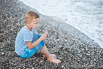 Boy in a striped t-shirt sitting close by the water at the beach Stock Photo