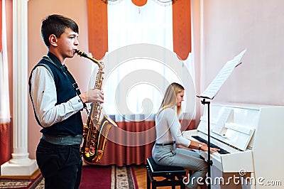 Boy student learns to play the saxophone in a music lesson to accompaniment of the piano Stock Photo