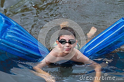 Boy swims on blue mattress in the river Stock Photo