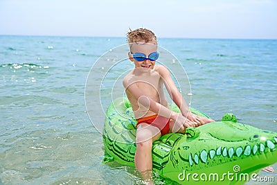 BOY SWIMS IN THE SEA ON THE INFLATABLE CROCODYLE TOY Stock Photo