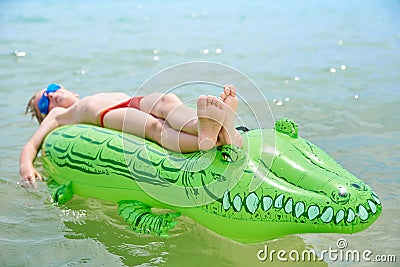 BOY SWIMS IN THE SEA ON THE INFLATABLE CROCODYLE TOY Stock Photo