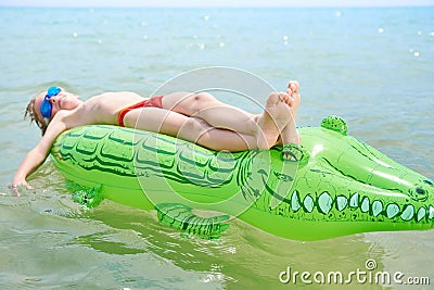 BOY SWIMS IN THE SEA ON THE CROCODYLE TOY Stock Photo