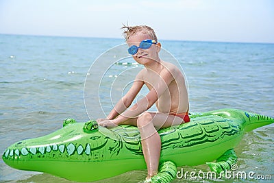 BOY SWIMS IN THE SEA ON INFLATABLE CROCODYLE TOY Stock Photo