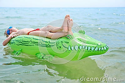 BOY SWIMS IN THE SEA ON THE INFLATABLE CROCODYLE TOY Stock Photo