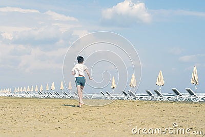 A boy in a T-shirt and shorts walks on the sandy Mackenzie beach in Larnaca. Cyprus Stock Photo