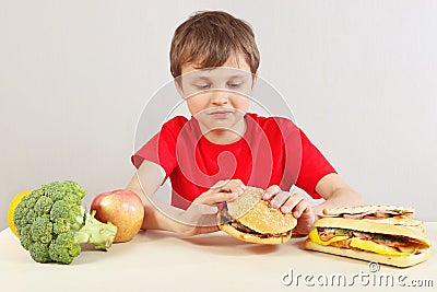 Boy at the table chooses between fastfood and healthy diet Stock Photo