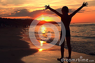 Boy takes a deep breath at the fiery sunset on the sea Stock Photo