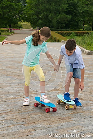 The boy teaches the girl to correctly stand on the skateboard on a walk in the city park Stock Photo