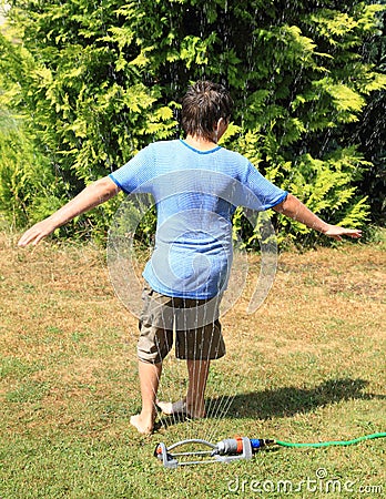 Boy twisting behind sprinkler Stock Photo