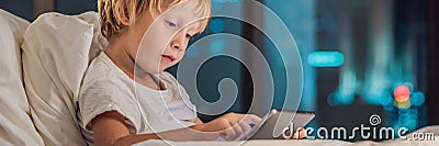 The boy uses the tablet in his bed before going to sleep on a background of a night city. Children and technology concepts BANNER, Stock Photo