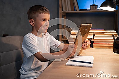 Boy using digital tablet while sitting on desk at home at night. Reading and studying Stock Photo