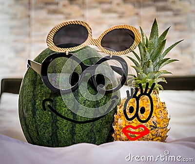 Boy Watermelon With Glasses And Girl Pineapple With Red Lips In Bed. Funny picture, couple having fun Stock Photo