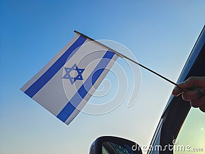 Boy waving Israel flag against the blue sky from the car window close-up shot. Man hand holding Israeli flag Stock Photo