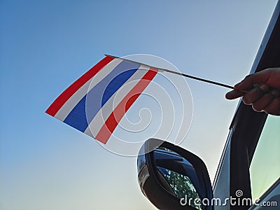 Boy waving Thailand flag against the blue sky from the car window close-up shot. Man hand holding Thai flag Stock Photo