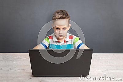 Boy works on a laptop computer and a desk. Concept of using computers for gaming and learning. Front view Stock Photo