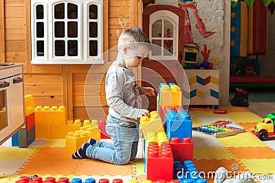 The boy is 4 years old, the blond plays on the playground indoors, builds a fortress from plastic blocks Stock Photo