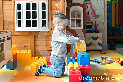 The boy is 4 years old, the blond plays on the playground indoors, builds a fortress from plastic blocks. Stock Photo