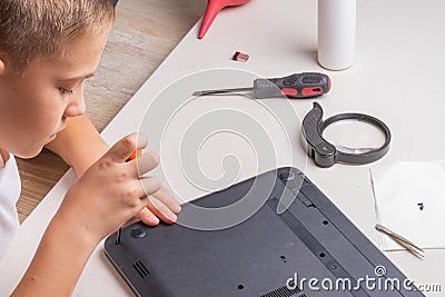 A boy of 10 years old is sorting a laptop for cleaning and maintenance. Selective focus. Screwdrivers, purge cylinder, magnifying Stock Photo