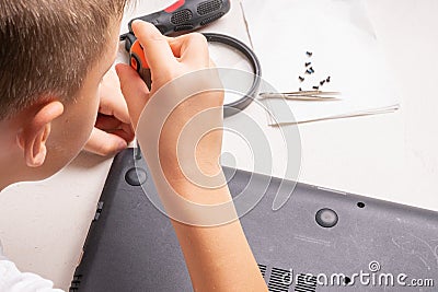 A boy of 10 years old is sorting a laptop for cleaning and maintenance. Selective focus. Screwdrivers, purge cylinder, magnifying Stock Photo