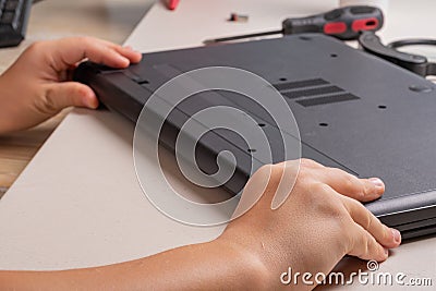 A boy of 10 years old is sorting a laptop for cleaning and maintenance. Selective focus. Screwdrivers, purge cylinder, magnifying Stock Photo