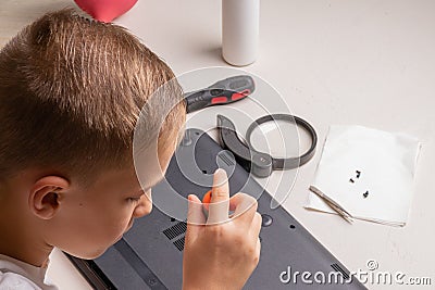 A boy of 10 years old is sorting a laptop for cleaning and maintenance. Selective focus. Screwdrivers, purge cylinder, magnifying Stock Photo