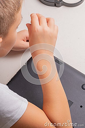 A boy of 10 years old is sorting a laptop for cleaning and maintenance. Selective focus. Screwdrivers, purge cylinder, magnifying Stock Photo