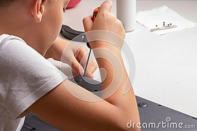 A boy of 10 years old is sorting a laptop for cleaning and maintenance. Selective focus. Screwdrivers, purge cylinder, magnifying Stock Photo