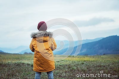 Boy in yellow coat looks on evening autumn mountain valley panorame Stock Photo