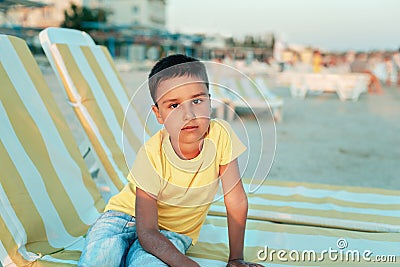 boy in yellow t-shirtsitting on bench near sea alone on beach at sunset. Happy family travel. Summer vacation with child Stock Photo