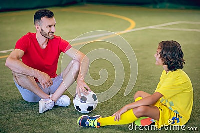 Boy in yellow uniform and his coach having a break after game Stock Photo