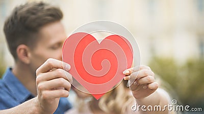Boyfriend and girlfriend cuddling and hiding behind paper heart, romantic love Stock Photo