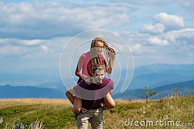 Boyfriend giving woman piggyback on traver. Man carrying woman on back in an summer nature. Stock Photo