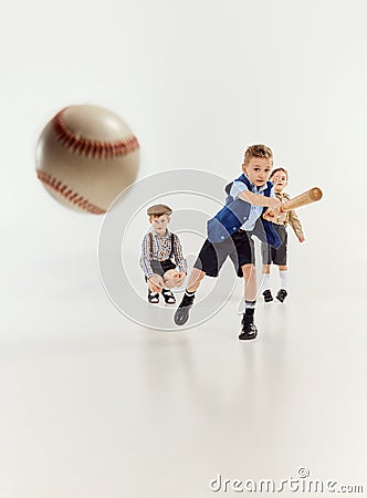 Boys, children in classical retro clothes playing baseball over grey studio background. Hitting. Competition. Concept of Stock Photo