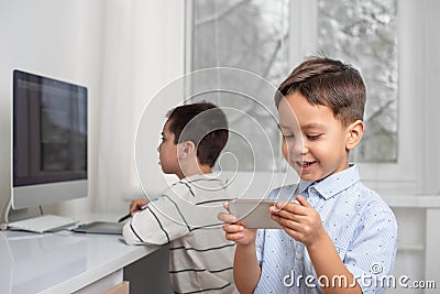 Boys enthusiastically draw on a computer using a tablet. The younger brother plays games on the phone Stock Photo