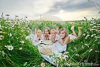 Boys and girls lie on a chamomile field. Children on a picnic in nature have fun among the flowers Stock Photo